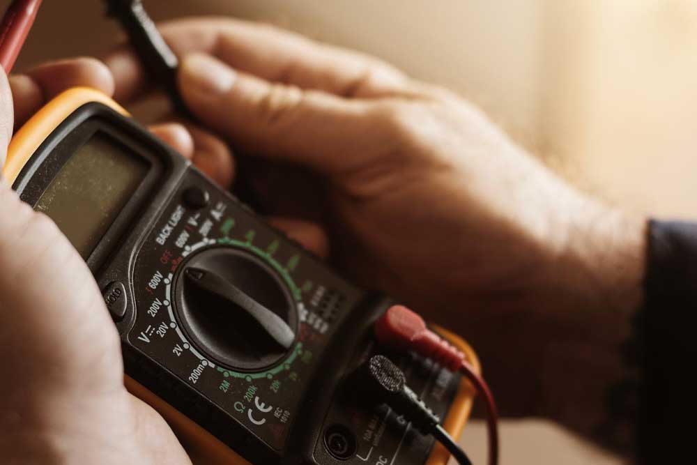 Nahaufnahme eines digitalen Multimeters in den Händen eines Technikers. Das Messgerät wird für die präzise Fehlerdiagnose bei elektrischen Defekten genutzt, um die genaue Ursache einer Störung schnell und sicher zu finden.