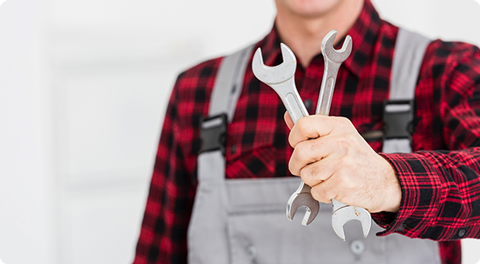 Oberkörper eines Technikers in Latzhose, der zwei Schrauebnschlüssel in einer Hand vorzeigt