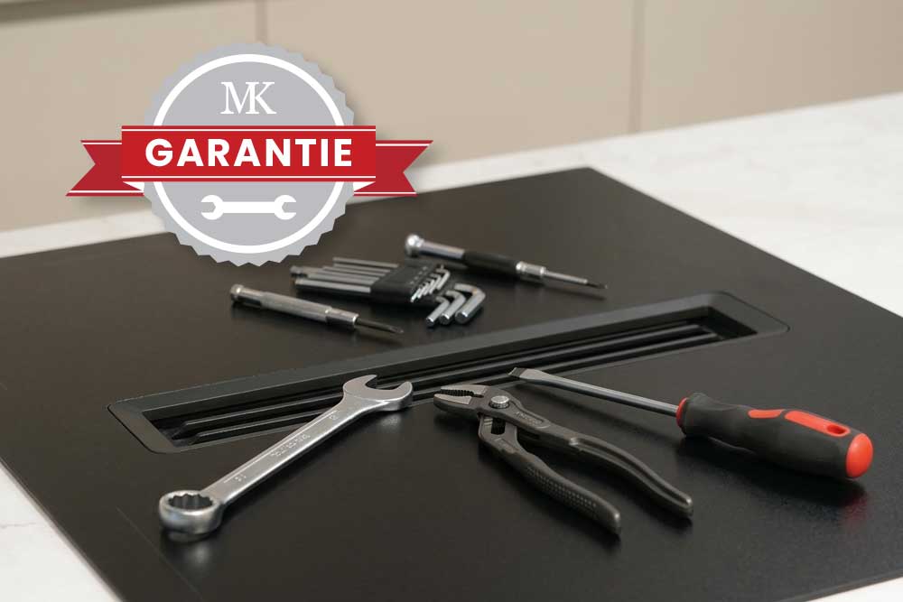 Nahaufnahme eines matten Kochfelds auf dem Werkzeuge liegen; im Vordergrund ist ein Siegel mit der Aufschrift 'MK Garantie'.