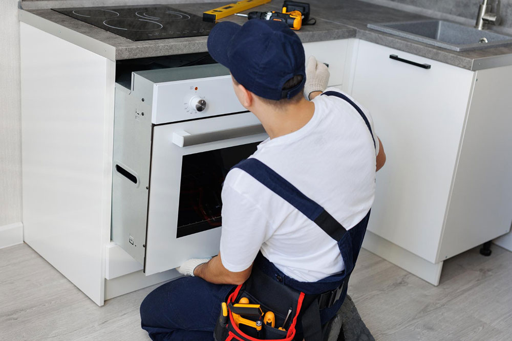 Techniker hockt in einer Küche und baut einen Backofen ein.